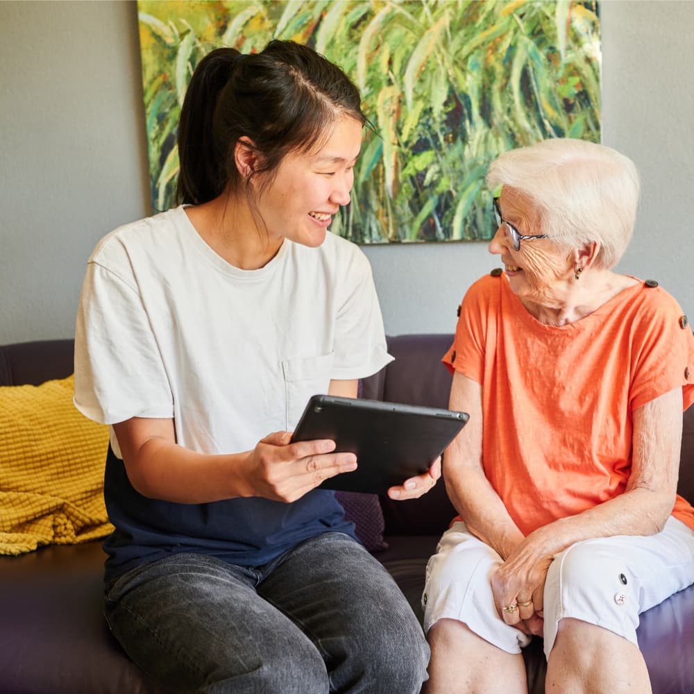 Een jonge vrouw toont een oudere vrouw iets op een tablet beide zitten op een bank