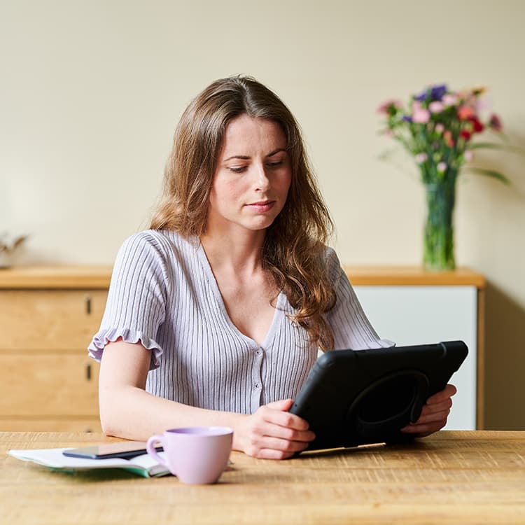 Een vrouw die aan de tafel zit met een tablet in haar handen